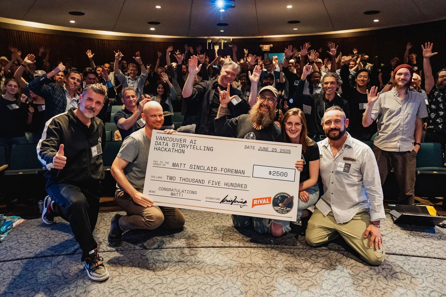 A hackathon prize cheque handoff with a full auditorium cheering behind the winners