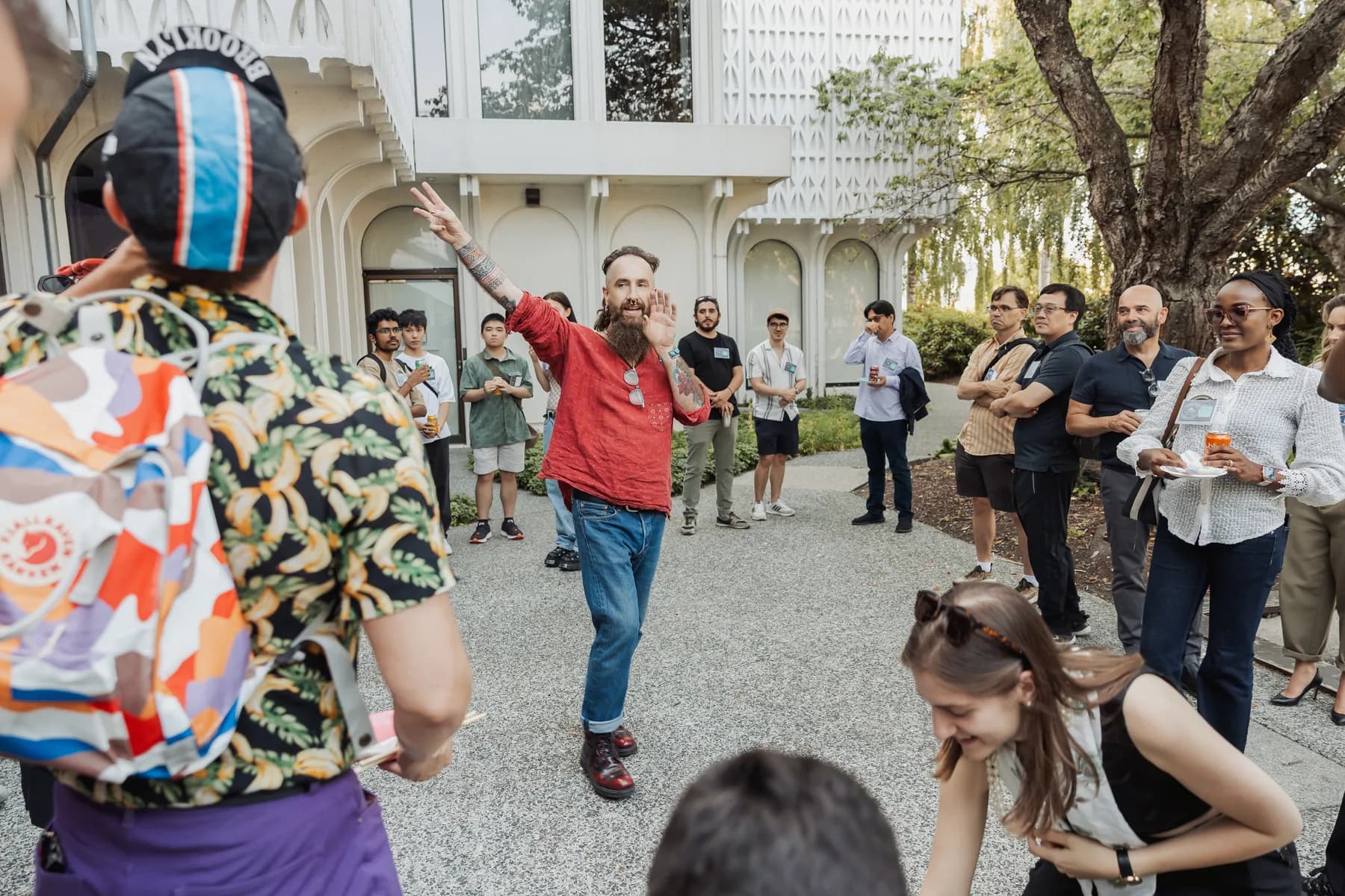 A man waving mid-gesture in an outdoor courtyard crowd at a Vancouver AI meetup