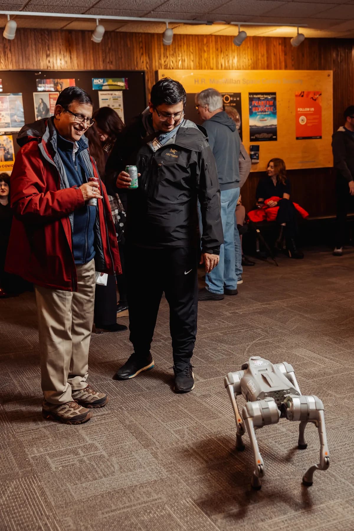 Two attendees watching the quadruped robot walk through the venue at a BC + AI community event.