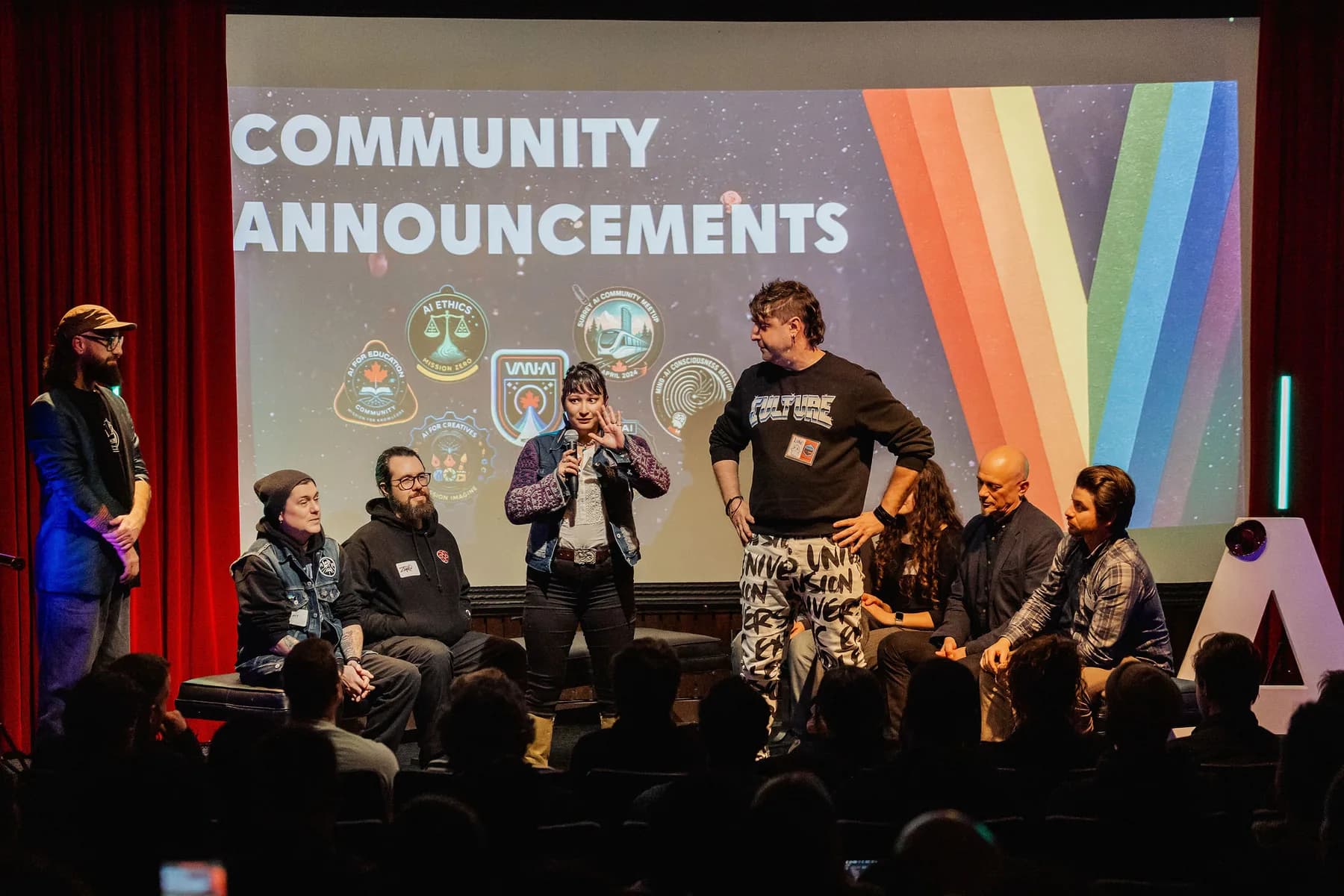 A seven-person community announcements panel on stage with a colourful Space Centre screen behind them
