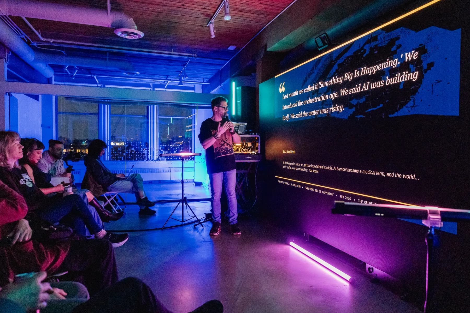 Speaker beside a vivid screen with the BC + AI Film Club audience in view