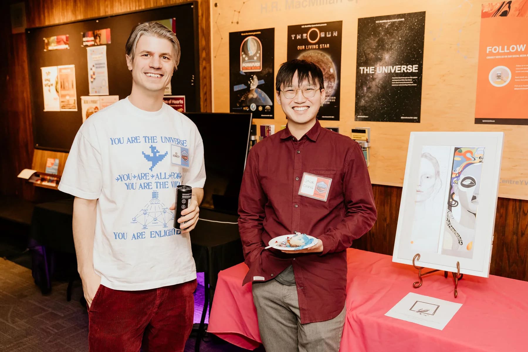 Two creators beside a table displaying artwork at a Vancouver AI community event.