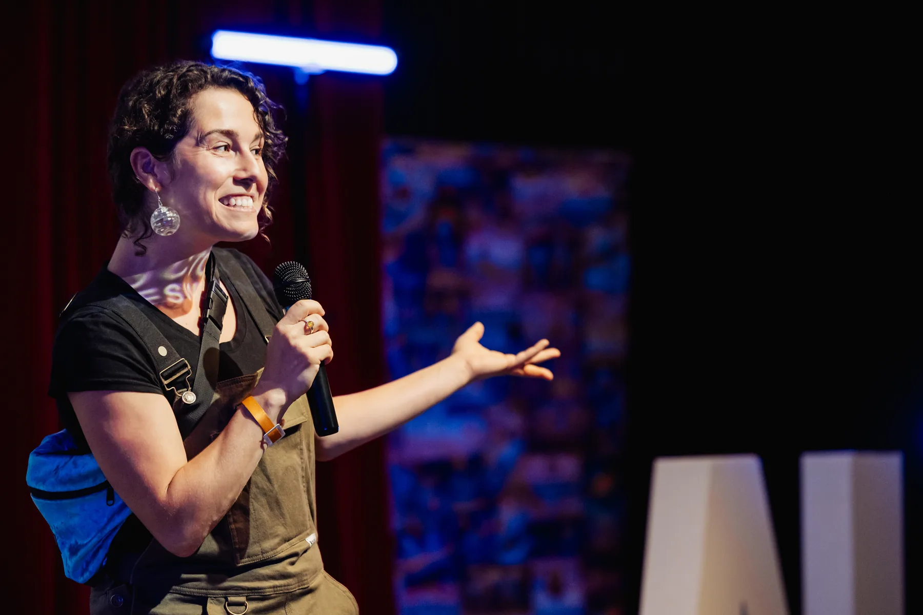 A speaker mid-gesture on stage with a microphone under warm blue stage lighting
