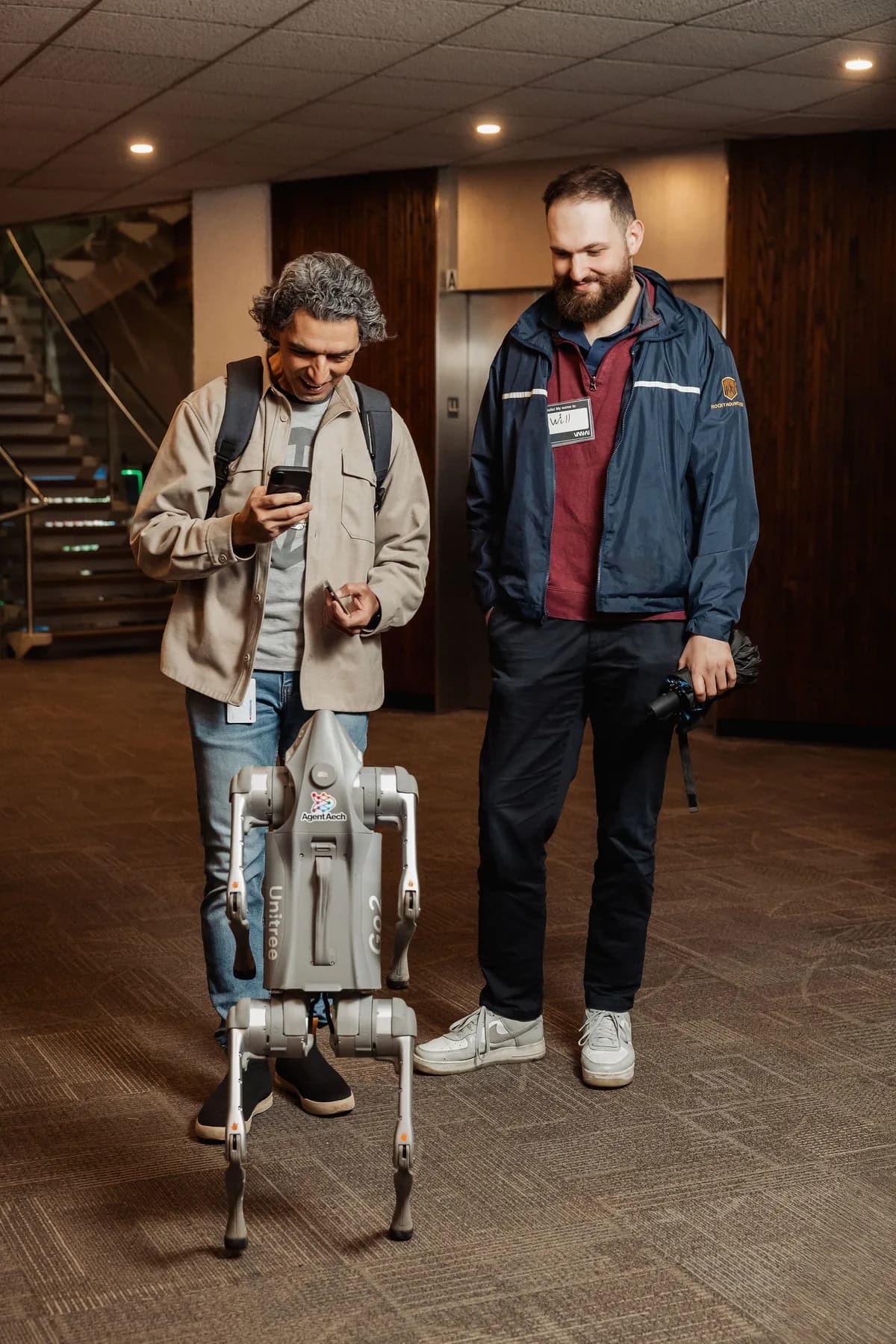 Two attendees trying a quadruped robot at a BC + AI community event.