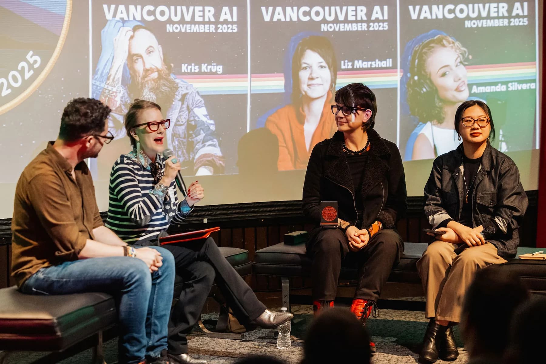 A panel conversation on stage with a Vancouver AI screen showing the night's speakers