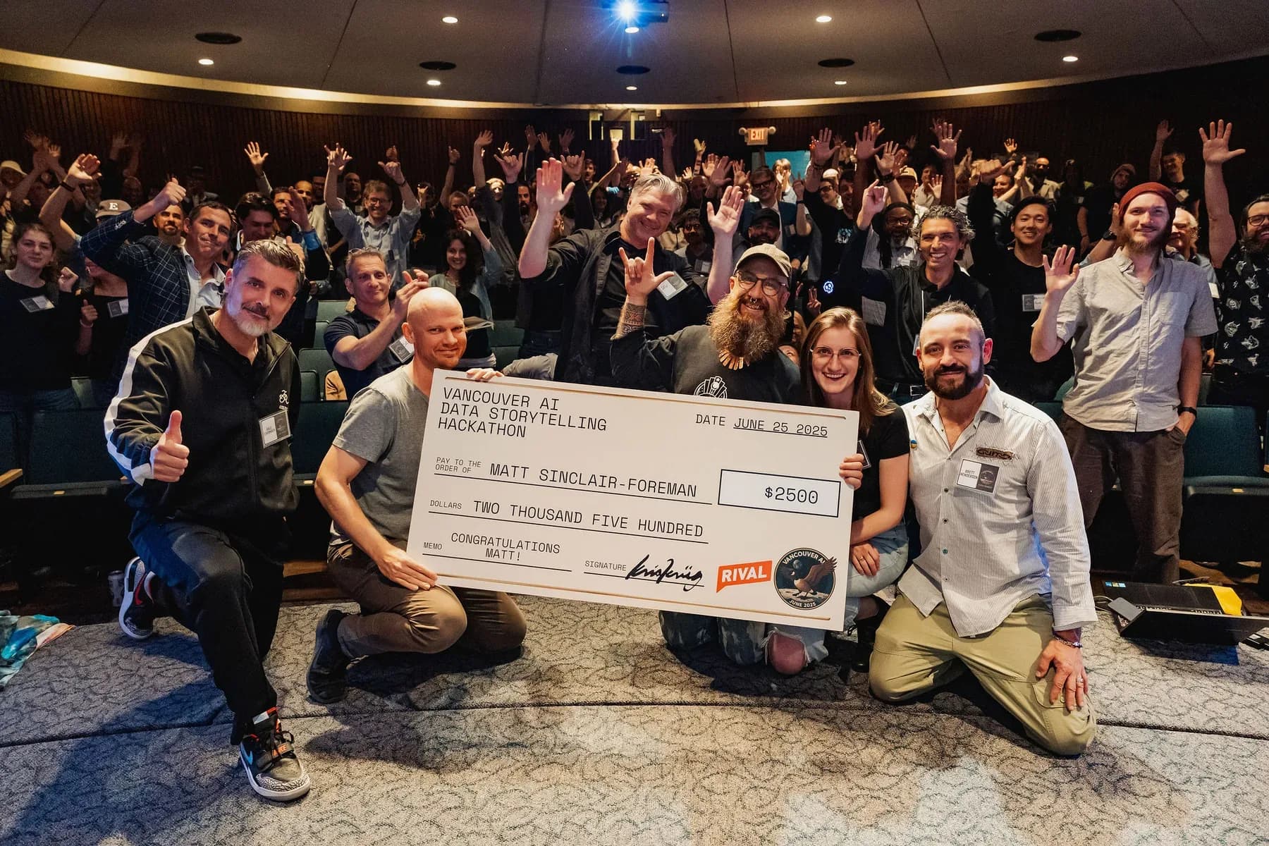Matt Sinclair-Foreman and organizers hold a 2,500 dollar Rival-sponsored hackathon cheque in front of a cheering Vancouver AI audience.