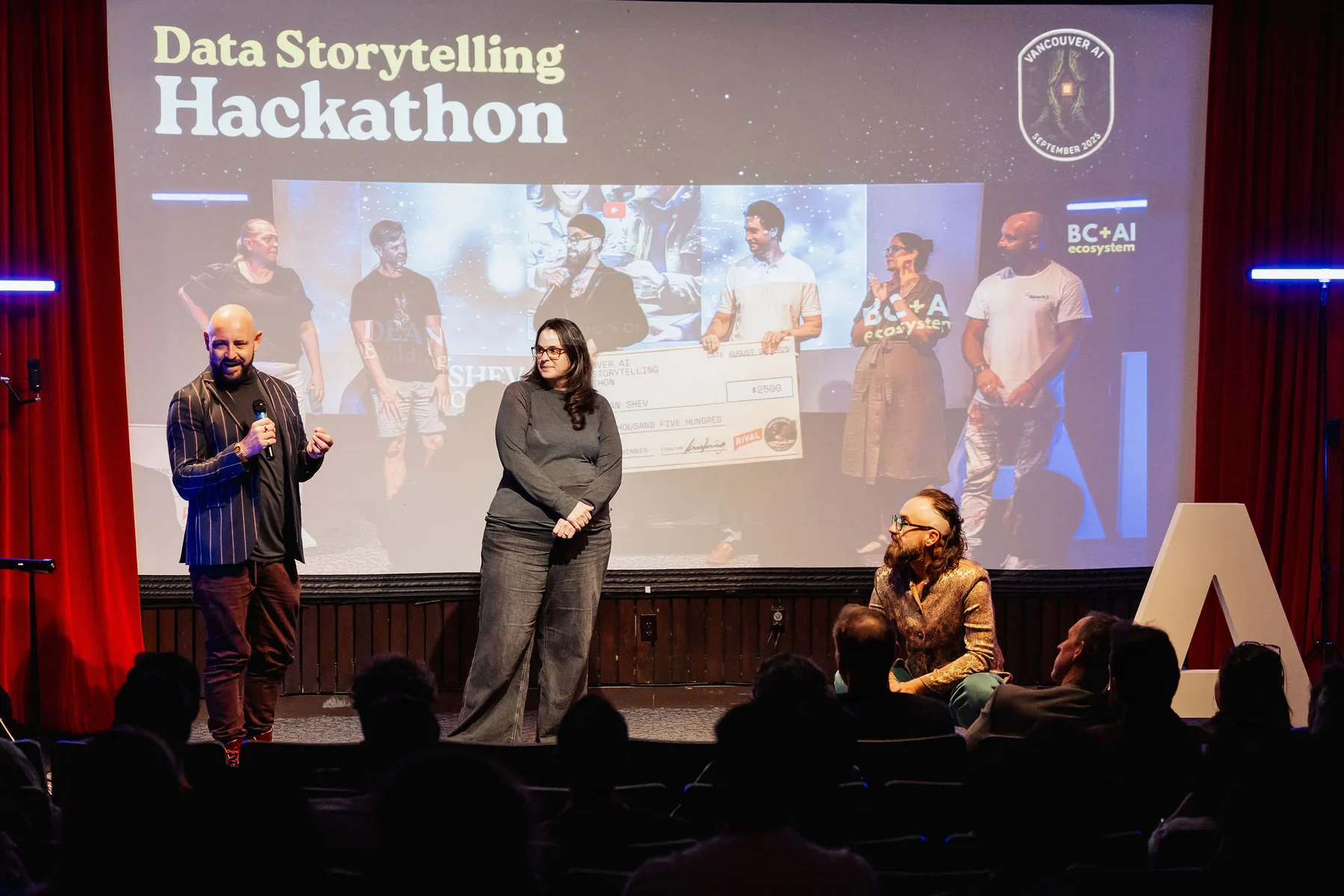 Vancouver AI Data Storytelling Hackathon stage with speakers and a Rival-sponsored winner cheque projected behind them.